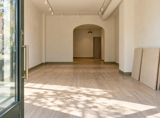 Illustrated empty shop with daylight across the floor and unfitted display panels beside a wall.